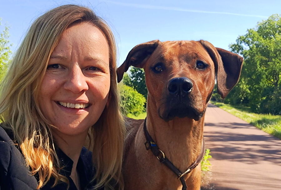 Eine lächelnde Frau posiert mit ihrem Hund auf einem Weg, ideal für die Ausbildung von Therapiebegleithunden.